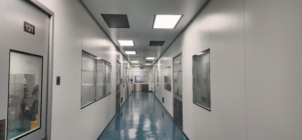 High-tech cleanroom facility with seamless white panel walls, glass observation windows, and a reflective blue floor for optimal cleanliness and efficiency.