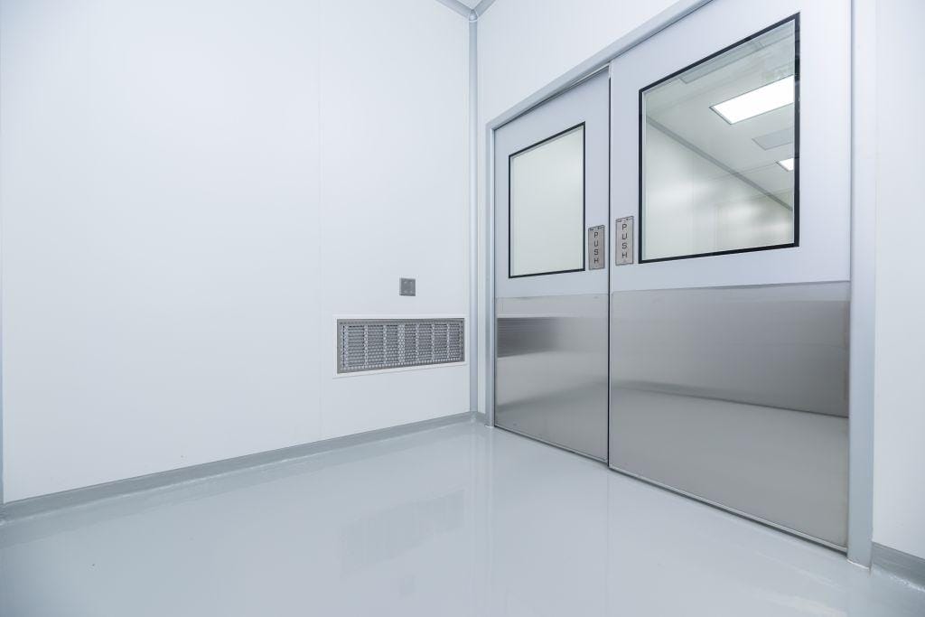 Cleanroom doors beside a wall return-air grille, showing the airflow balance behind door-related pressure failures