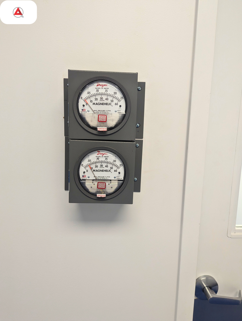 Dual Magnehelic differential pressure gauges mounted on a modular cleanroom wall panel next to an airlock door